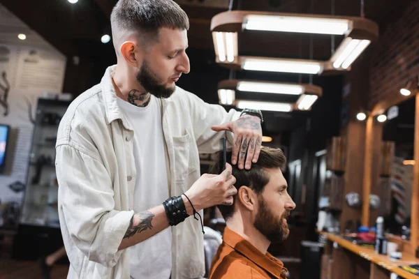 Barbeiro pentear o cabelo do cliente barbudo na barbearia — Fotografia de Stock