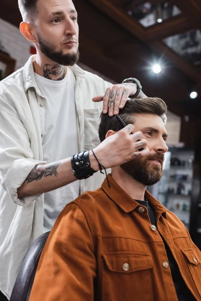 Tatoué coiffeur peignage cheveux de l'homme heureux dans le salon de coiffure — Photo de stock