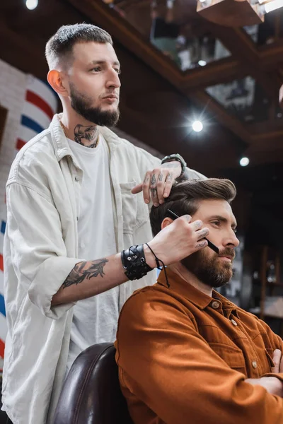 Tätowierter Friseur kämmt Haare bärtiger Kundin im Salon — Stockfoto