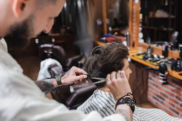 Barbeiro desfocado corte de cabelo do homem na capa de cabeleireiro na barbearia — Fotografia de Stock