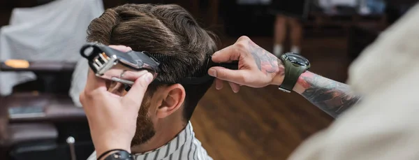 Tatuado barbeiro pentear e aparar o cabelo do homem na barbearia, banner — Fotografia de Stock