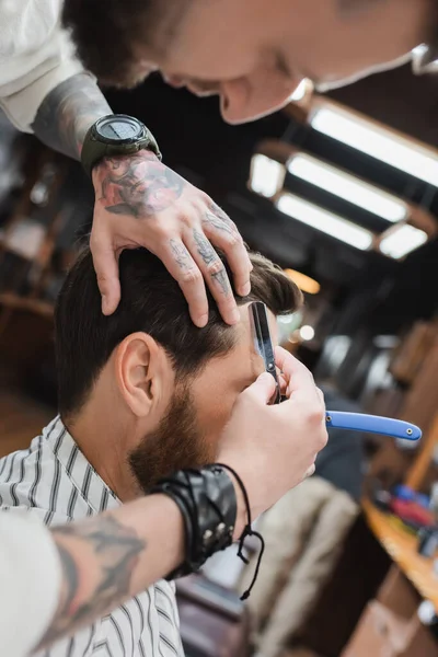 Barbeiro desfocado aparar o cabelo do cliente com navalha reta na barbearia — Fotografia de Stock