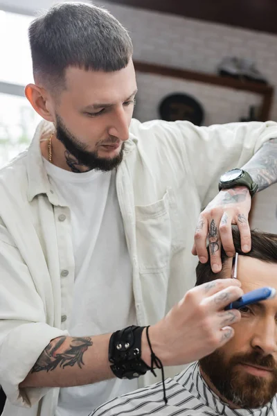 Bearded barber shaving forehead of client with straight razor — Stock Photo
