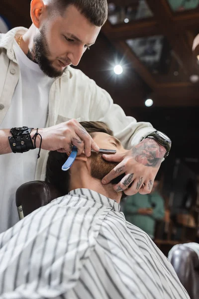 Vista basso angolo di barba da barba parrucchiere tatuato dell'uomo con rasoio dritto — Foto stock