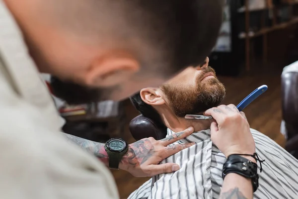 Cabeleireiro desfocado raspando pescoço do cliente com navalha reta na barbearia — Stock Photo