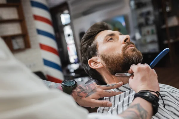 Peluquero tatuado en el cliente de afeitar reloj de pulsera con afeitadora recta - foto de stock