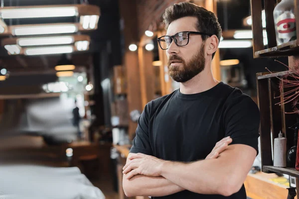 Confident hairstylist in eyeglasses crossing arms in barbershop — Stock Photo