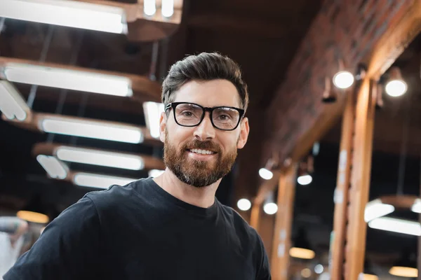 Uomo sorridente in t-shirt e occhiali che guarda la fotocamera nel salone di bellezza — Foto stock