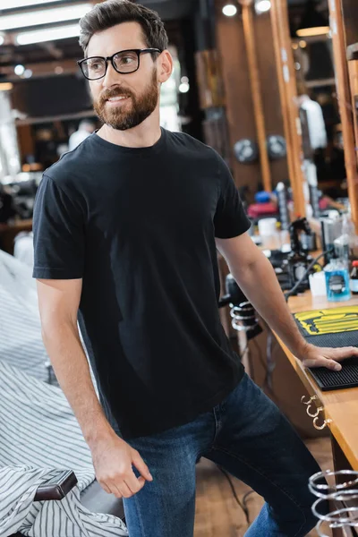 Cheerful client in eyeglasses looking away near worktop in barbershop — Stock Photo