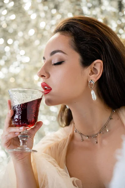 Sexy morena mujer con maquillaje celebración vaso de vino tinto sobre fondo brillante - foto de stock