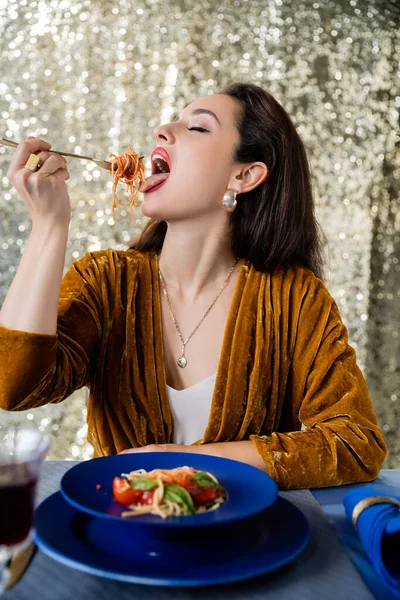 Elegant brunette woman eating delicious pasta near blue plates on glitter silver background — Stock Photo