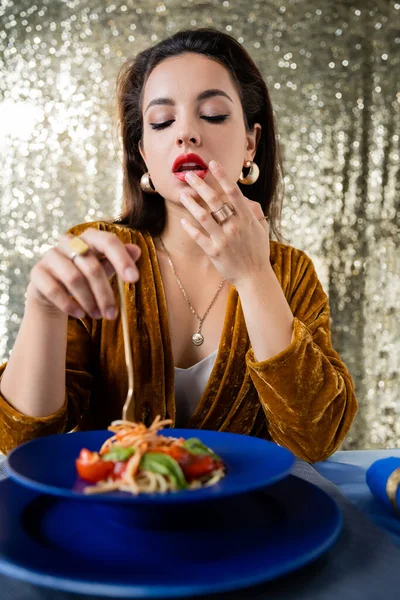 Femme sexy en robe élégante toucher lèvre près de plaque floue avec des pâtes sur fond pailleté — Photo de stock