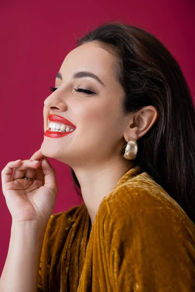 Portrait of brunette woman with closed eyes and makeup smiling isolated on red — Stock Photo