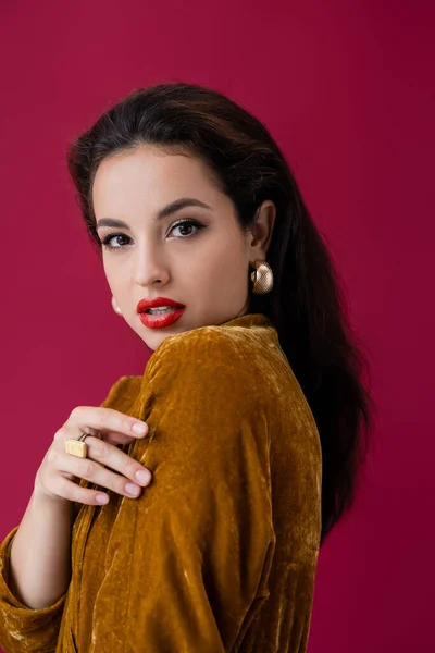 Sensual woman in earrings and velour dress looking at camera isolated on red — Stock Photo