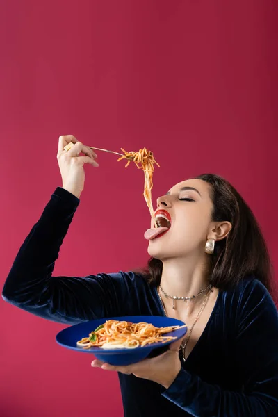 Brünette Frau im Velourkleid isst leckere Spaghetti von blauem Teller auf rotem — Stockfoto