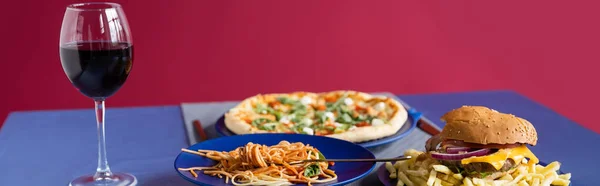 Blauer Tisch mit Weinglas neben Tellern mit leckerem Essen isoliert auf rotem, Banner — Stockfoto