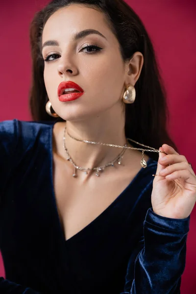 Glamour woman with red lips touching necklace and looking at camera isolated on burgundy — Stock Photo