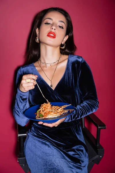 Sexy donna in velluto vestito tenendo piatto blu con deliziosi spaghetti su sfondo rosso — Foto stock