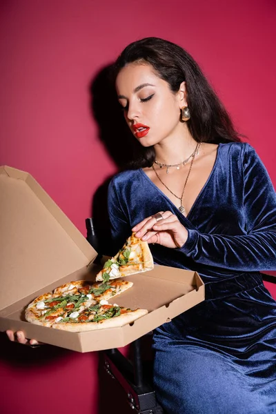 Morena elegante mulher tomando pedaço de pizza de caixa de papelão no fundo vermelho — Fotografia de Stock