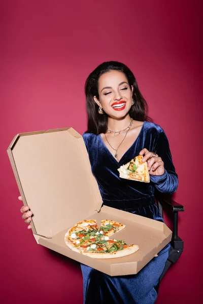 Cheerful stylish woman holding carton box of delicious pizza on red background — Stock Photo