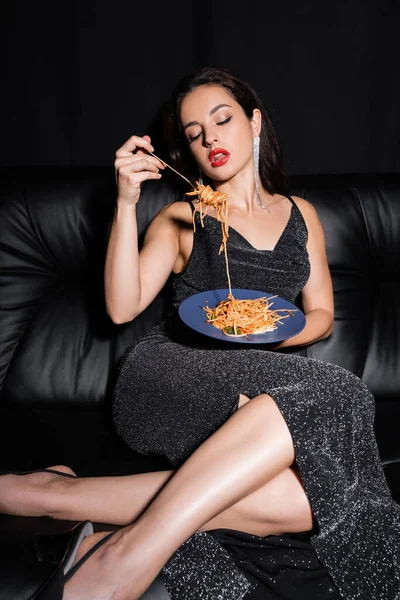 Sexy woman in elegant lurex dress eating delicious spaghetti isolated on black — Stock Photo