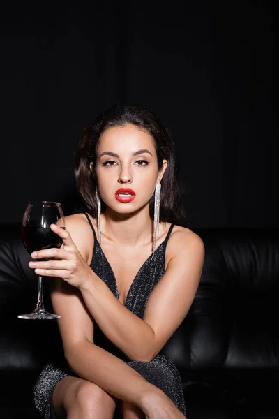 Mujer sexy y elegante con copa de vino mirando a la cámara aislada en negro - foto de stock