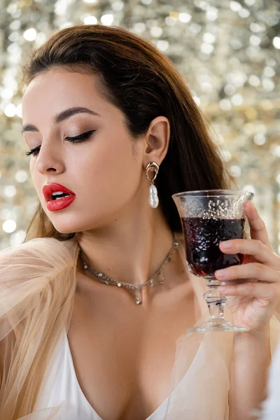 Young and sensual woman with makeup holding glass of red wine on shiny background — Stock Photo