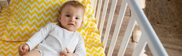 Von oben: niedliches Säuglingsmädchen im Babystrampler liegend auf gelbem Bettzeug im Kinderbett, Banner — Stockfoto