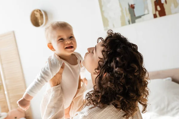 Curly woman in loungewear holding in arms baby daughter in romper — Stock Photo