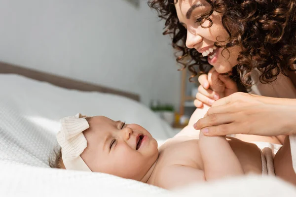 Joyeuse mère avec les cheveux bouclés tenant les mains de bébé fille dans le bandeau — Photo de stock