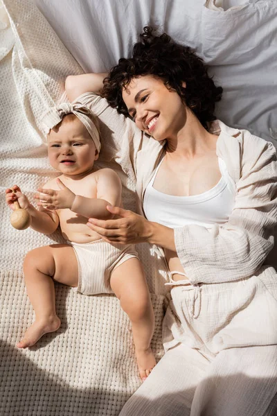 Вид сверху на счастливую мать лежащую на кровати с маленькой девочкой в ободке с луком — стоковое фото