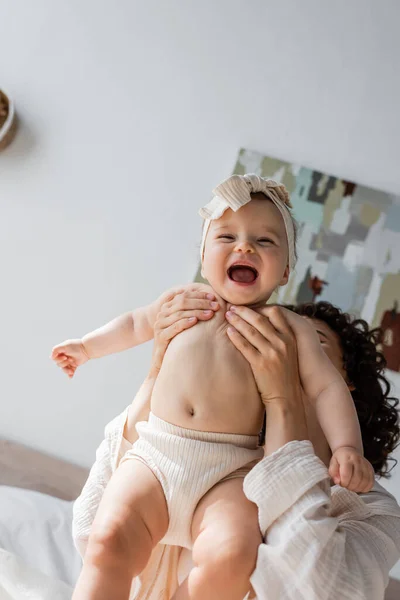 Mulher encaracolado segurando bebê animado filha na cabeça com arco e roupa interior — Fotografia de Stock