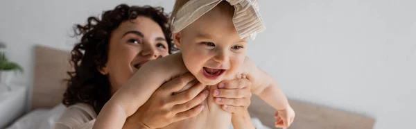 Curly woman holding happy infant daughter in headband with bow, banner — Stock Photo