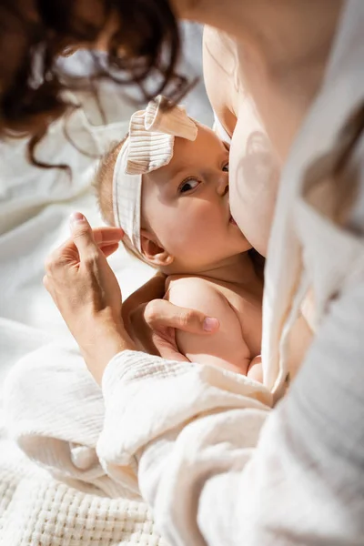 High angle view of curly woman breastfeeding infant daughter in headband with bow — Stock Photo