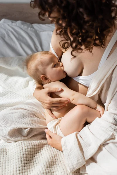 High angle view of curly mother in loungewear breastfeeding infant daughter — Stock Photo