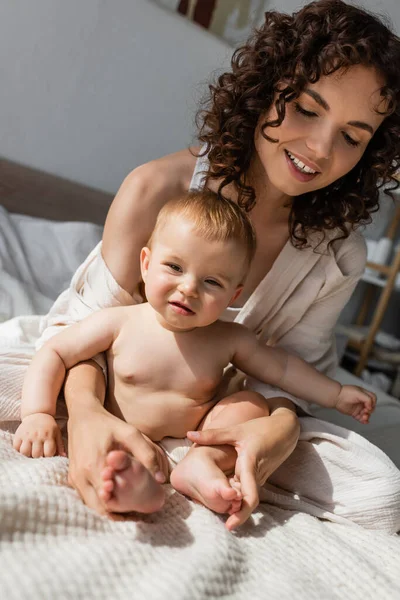 Cheerful mother in loungewear sitting with infant child on bed — Stock Photo