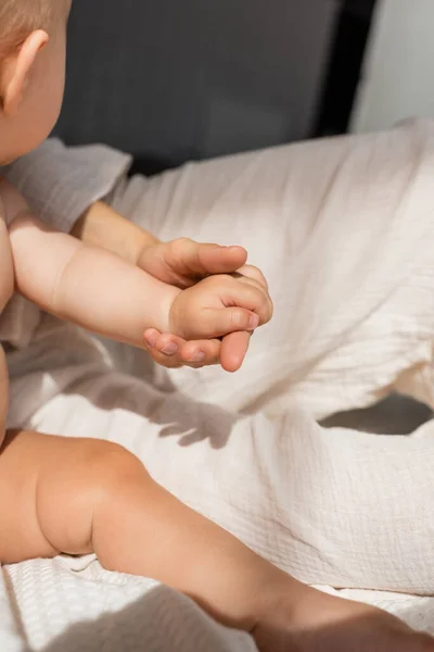 Cropped view of mother holding hands with cute baby girl in bedroom — Stock Photo