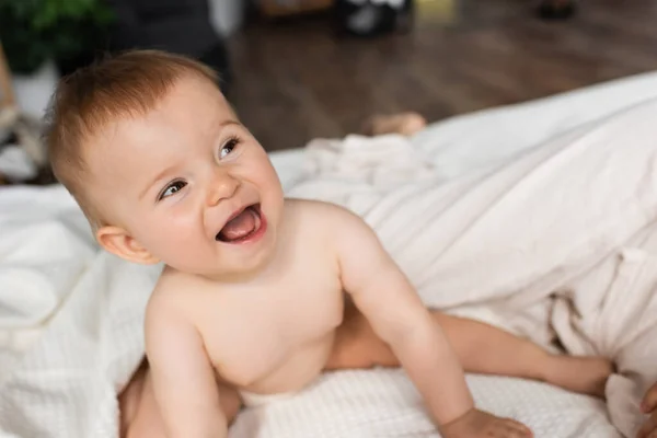 Высокий угол зрения счастливого младенца с открытым ртом, сидящего на кровати — стоковое фото