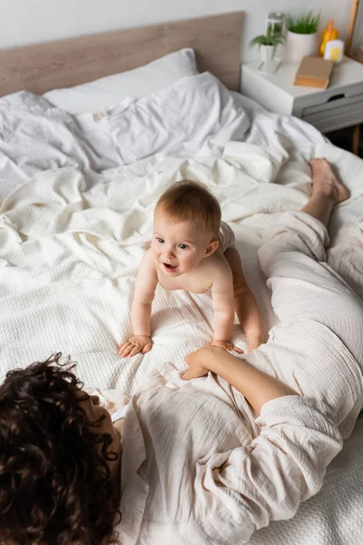 Top view of amazed infant kid looking at curly mother resting on bed — Stock Photo