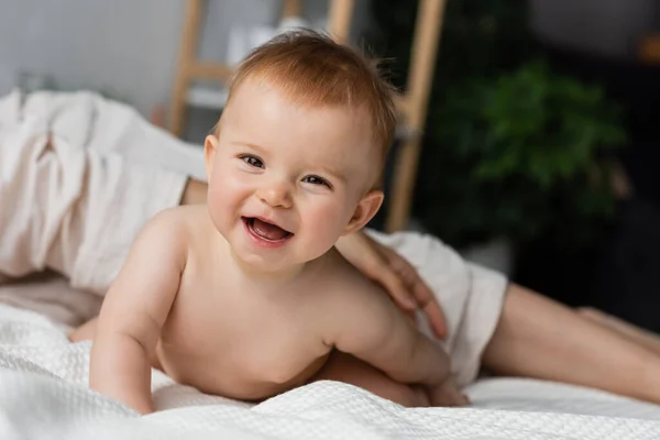 Mutter in der Nähe glücklicher Säuglingstochter blickt in Kamera im Schlafzimmer — Stockfoto