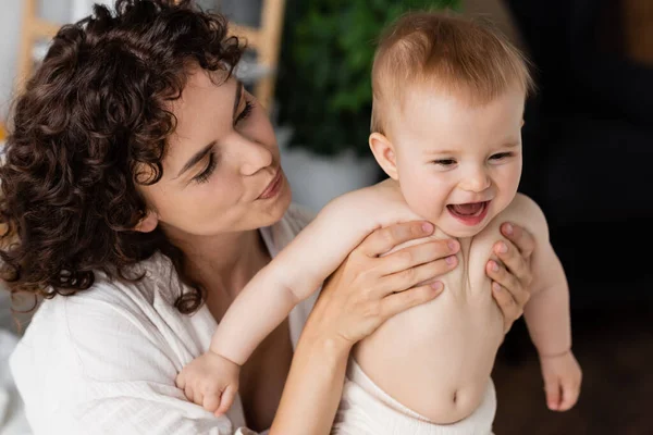 Mulher com cabelo encaracolado segurando nos braços bebê infantil animado com boca aberta — Fotografia de Stock