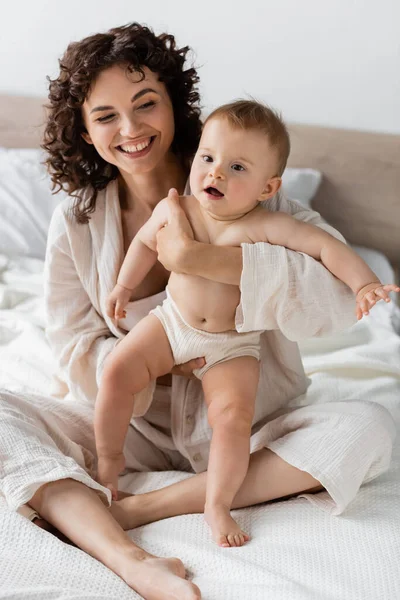 Mujer alegre en ropa de salón sosteniendo en brazos hija bebé sorprendido con la boca abierta - foto de stock