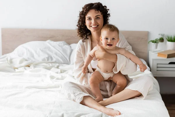 Joyful woman in loungewear holding in arms amazed baby daughter with opened mouth — Stock Photo