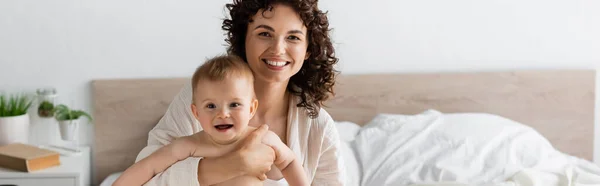 Mujer alegre en ropa de salón sosteniendo en brazos hija bebé sorprendido con la boca abierta, pancarta - foto de stock