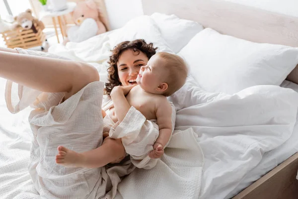 Vue du dessus de la femme heureuse en vêtements de salon couché sur le lit avec la fille de bébé gaie — Photo de stock