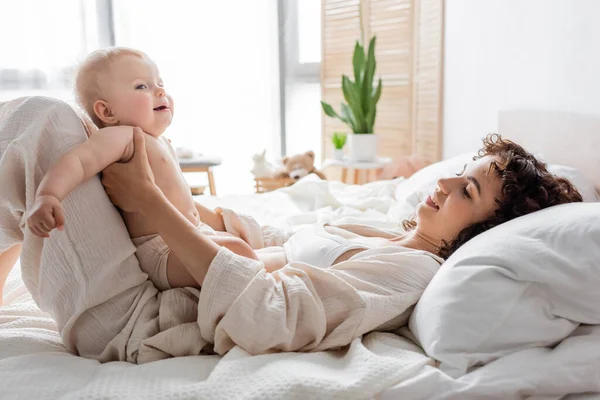 Femme heureuse en vêtements de salon couché sur le lit avec bébé fille mignonne — Photo de stock