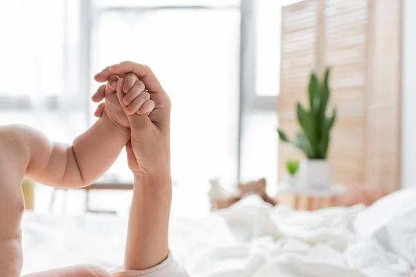 Vista recortada de la madre sosteniendo diminuta mano de hija lactante en casa - foto de stock