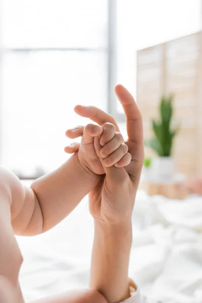 Cropped view of child holding finger of mother in blurred bedroom — Stock Photo