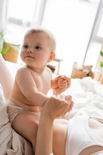Woman holding hands of baby daughter on bed in morning — Stock Photo