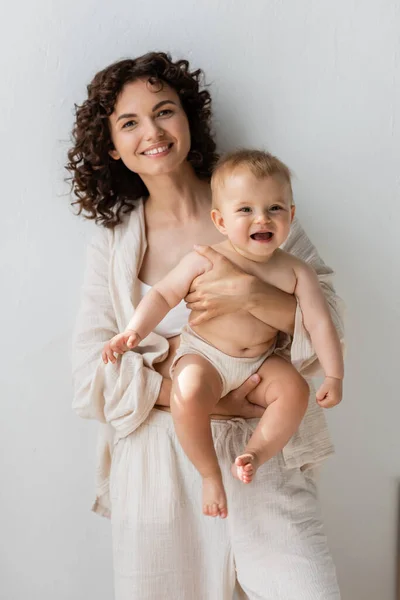 Позитивна брюнетка мама в піжамі тримає дівчинку вдома — стокове фото